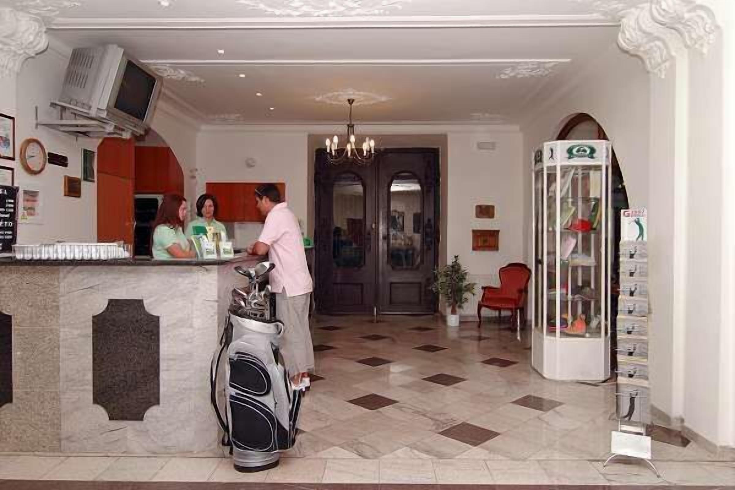 A hotel reception area with a counter, a television mounted above it, and a golf bag placed on the floor.
