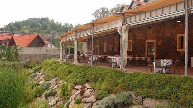 Un restaurante con terraza, paredes de piedra y un paisaje de colinas al fondo.