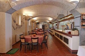 A restaurant with tables covered in checkered tablecloths, a bar area with bottles, and a tiled floor. - Golf Resort Hotel Konopiste (Bystrice)