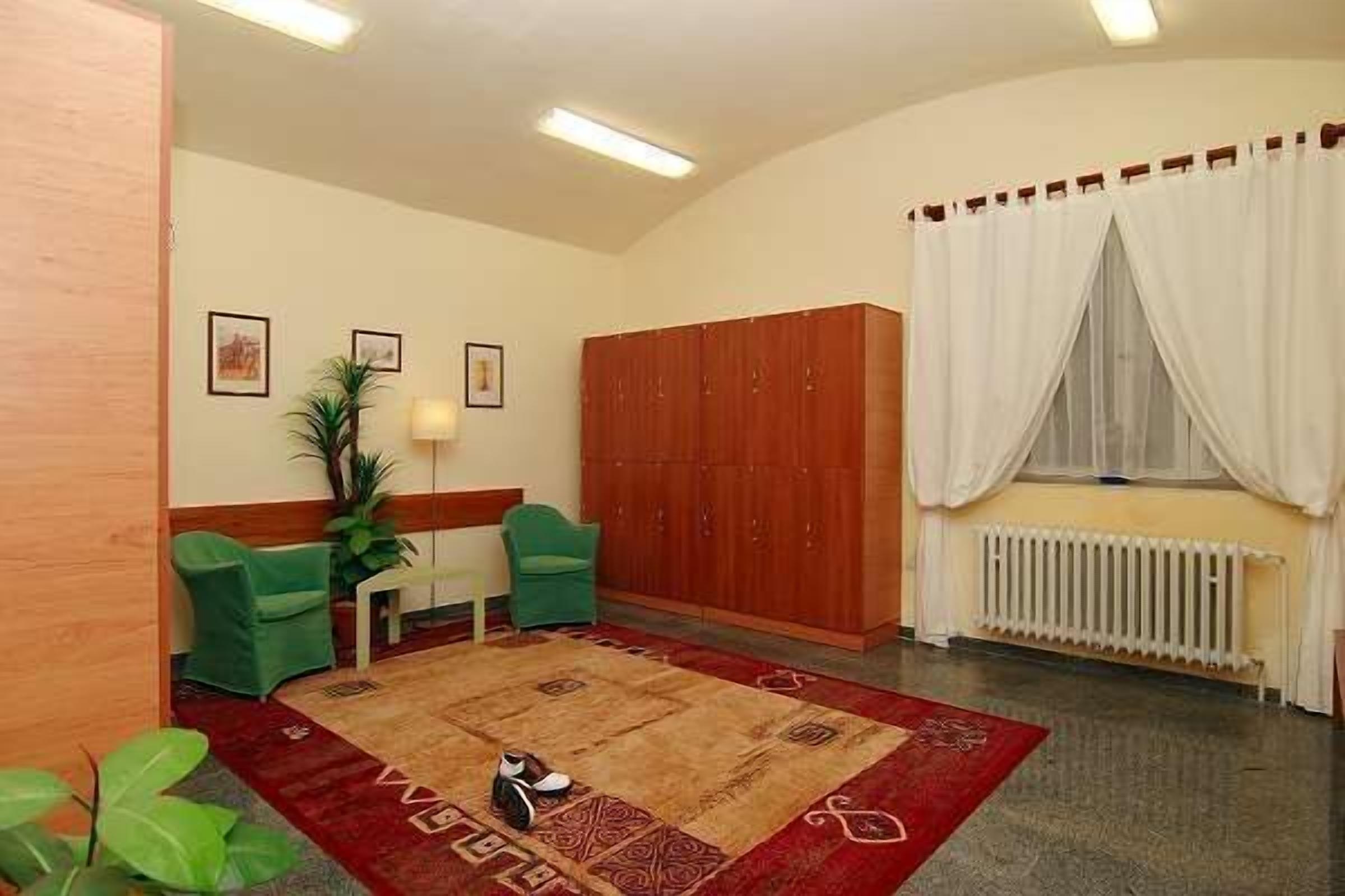 Una habitación con un armario de madera, dos sillas verdes, un radiador y un tapete de diseño rojo y beige.