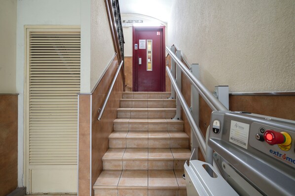 A staircase with beige tiles, a red door at the top, and a handrail on the right.