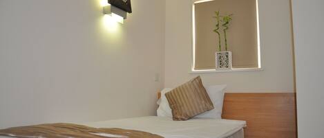 A neatly made bed with a striped blanket, a wooden headboard, and a wall-mounted light fixture.