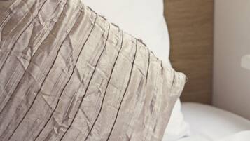A bed with a single beige pillow and a wooden nightstand beside it.