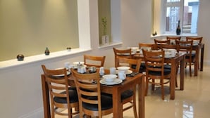 A dining area with multiple wooden tables and chairs, arranged in a spacious room with a large window providing natural light.