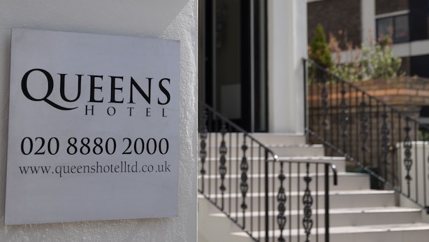 A sign for Queens Hotel with contact information and website URL.