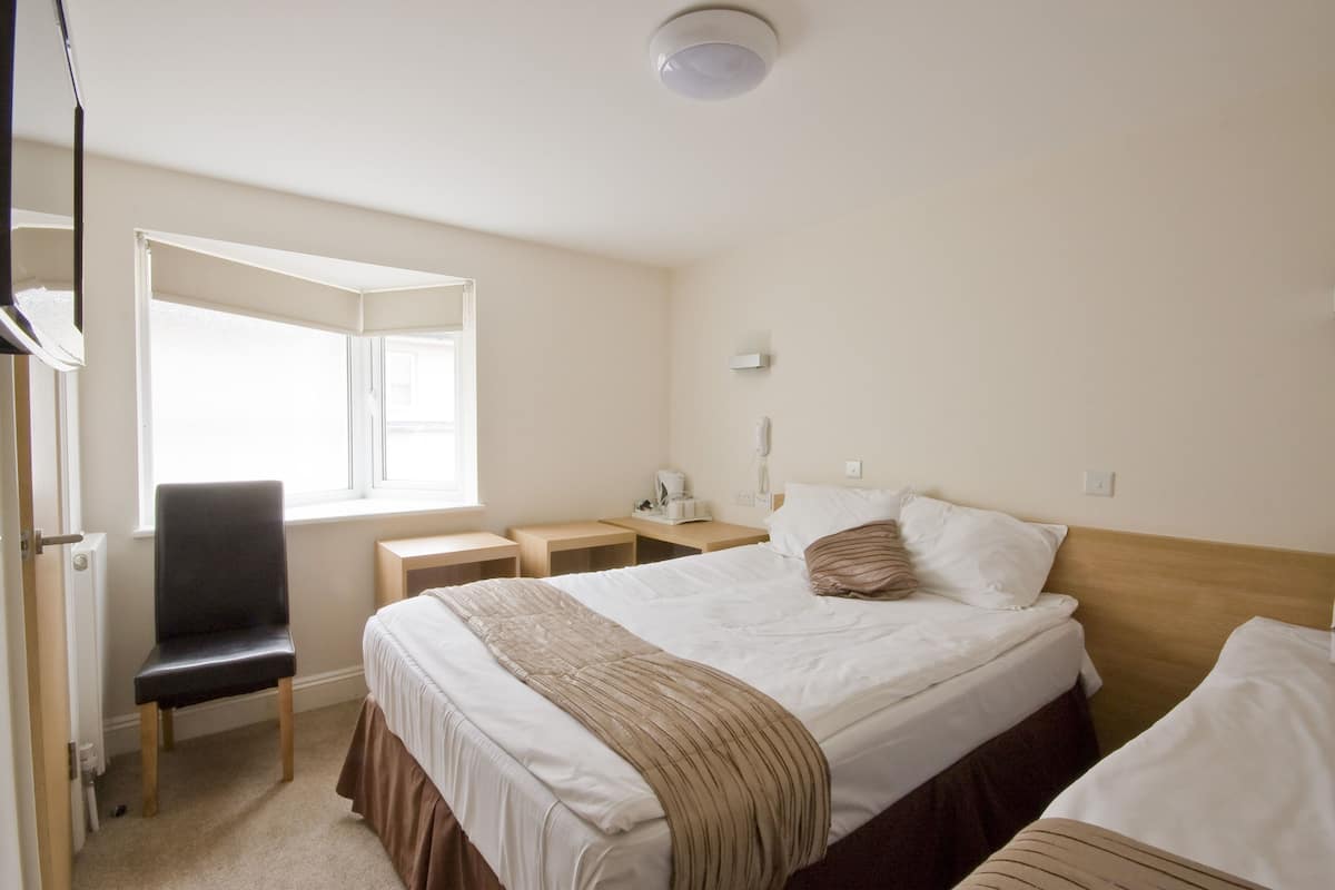 A hotel room with two beds, a chair, a desk, and a window.