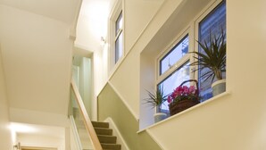 A carpeted staircase with a wooden handrail, a small window with potted plants, and a door at the top.