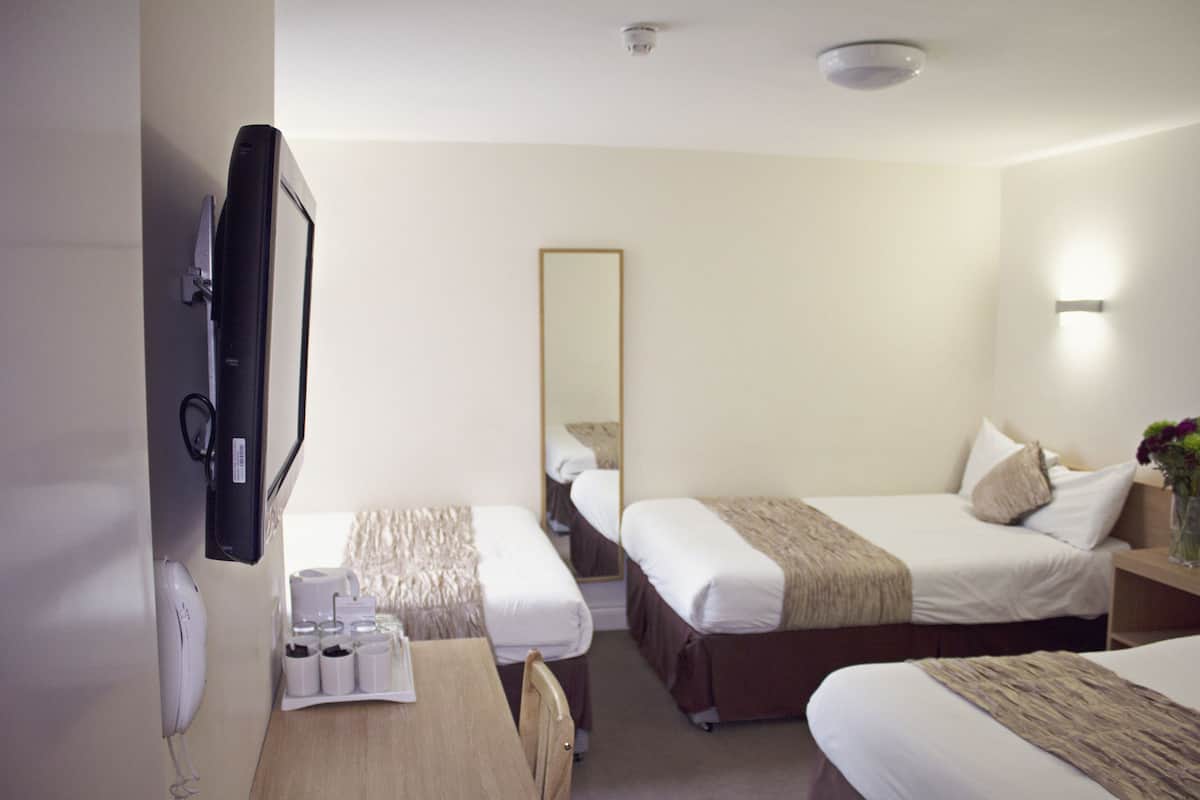 A hotel room with two single beds, a desk with a chair, a flat-screen TV mounted on the wall, a bedside table with a vase of flowers, and a mirror on the wall.