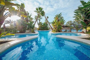 A swimming pool with clear blue water, surrounded by tropical plants and palm trees.