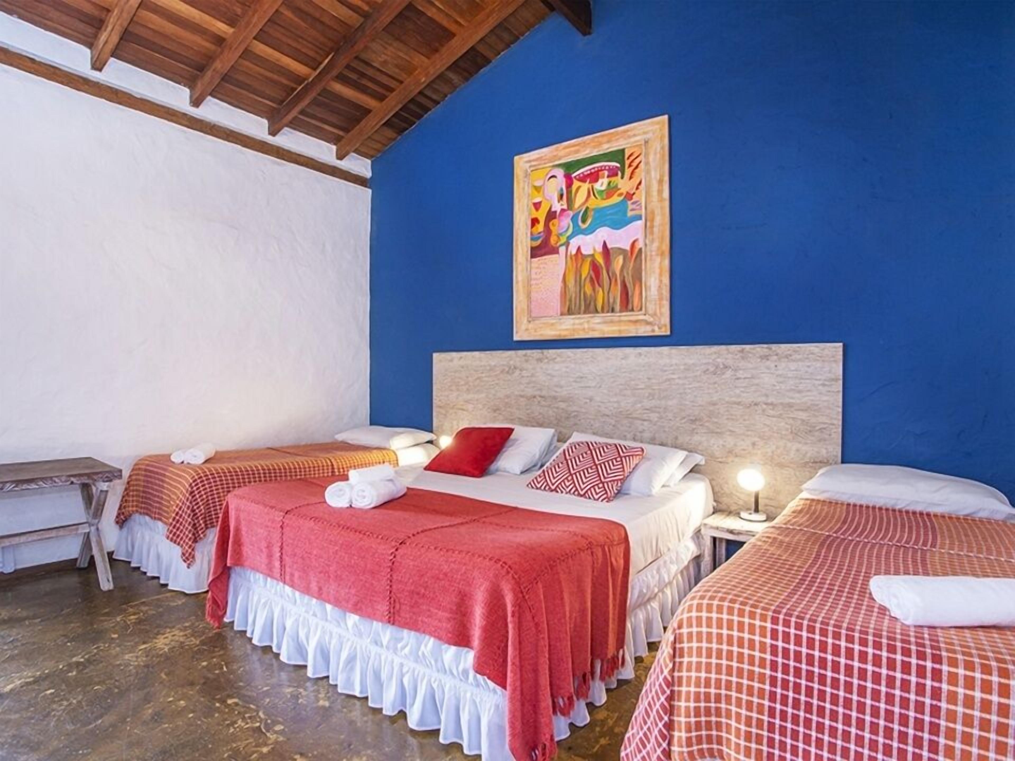 A hotel room with two beds, each with a red and white checkered bedspread, a wooden headboard, and a painting on the blue wall.