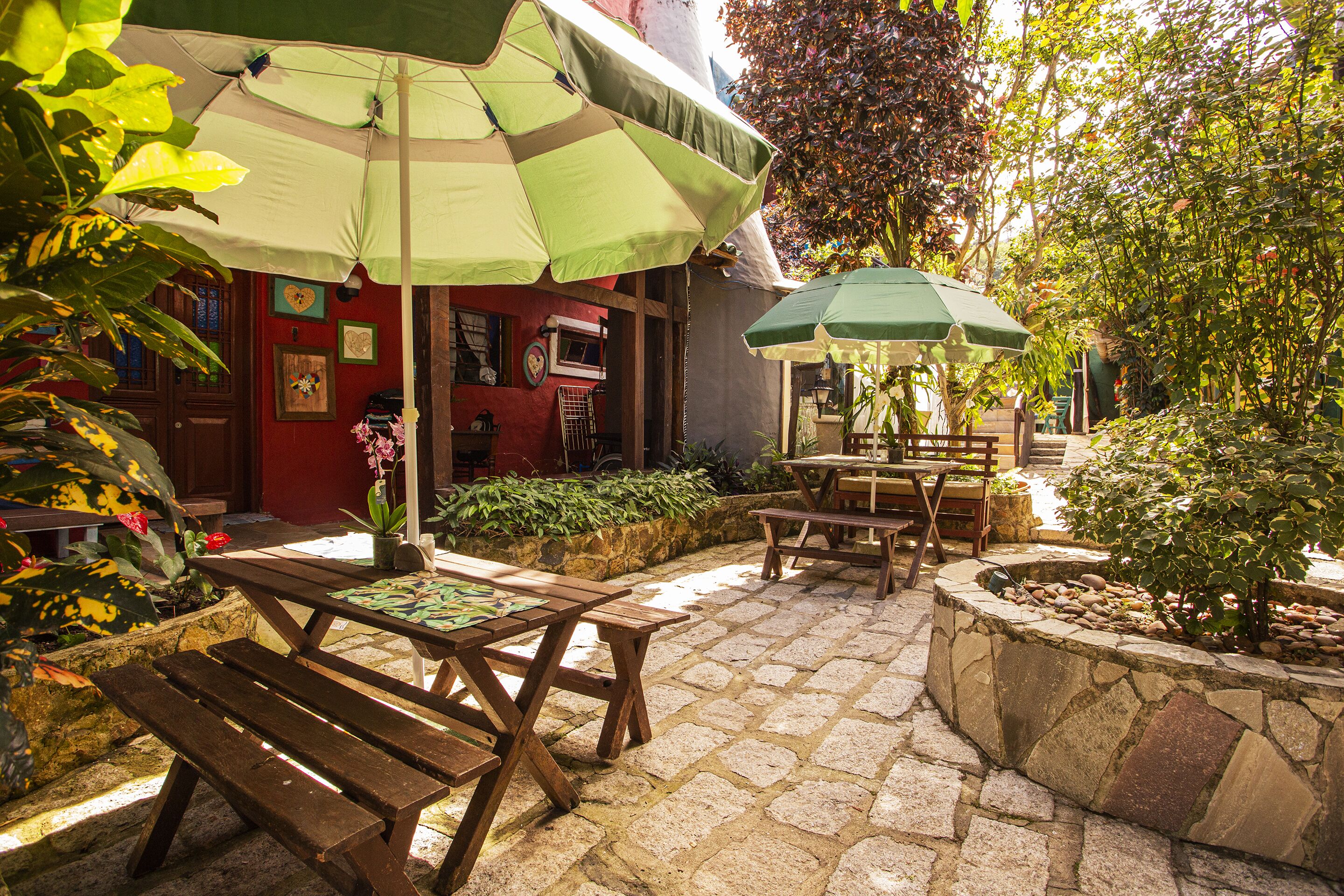 An outdoor patio with stone flooring, wooden tables and benches, and green umbrellas providing shade.