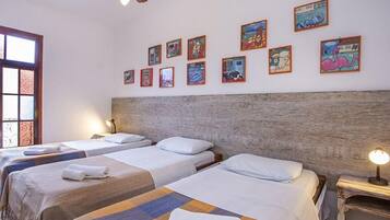 Une chambre d’hôtel avec trois lits simples, une tête de lit en bois et un ventilateur de plafond.
