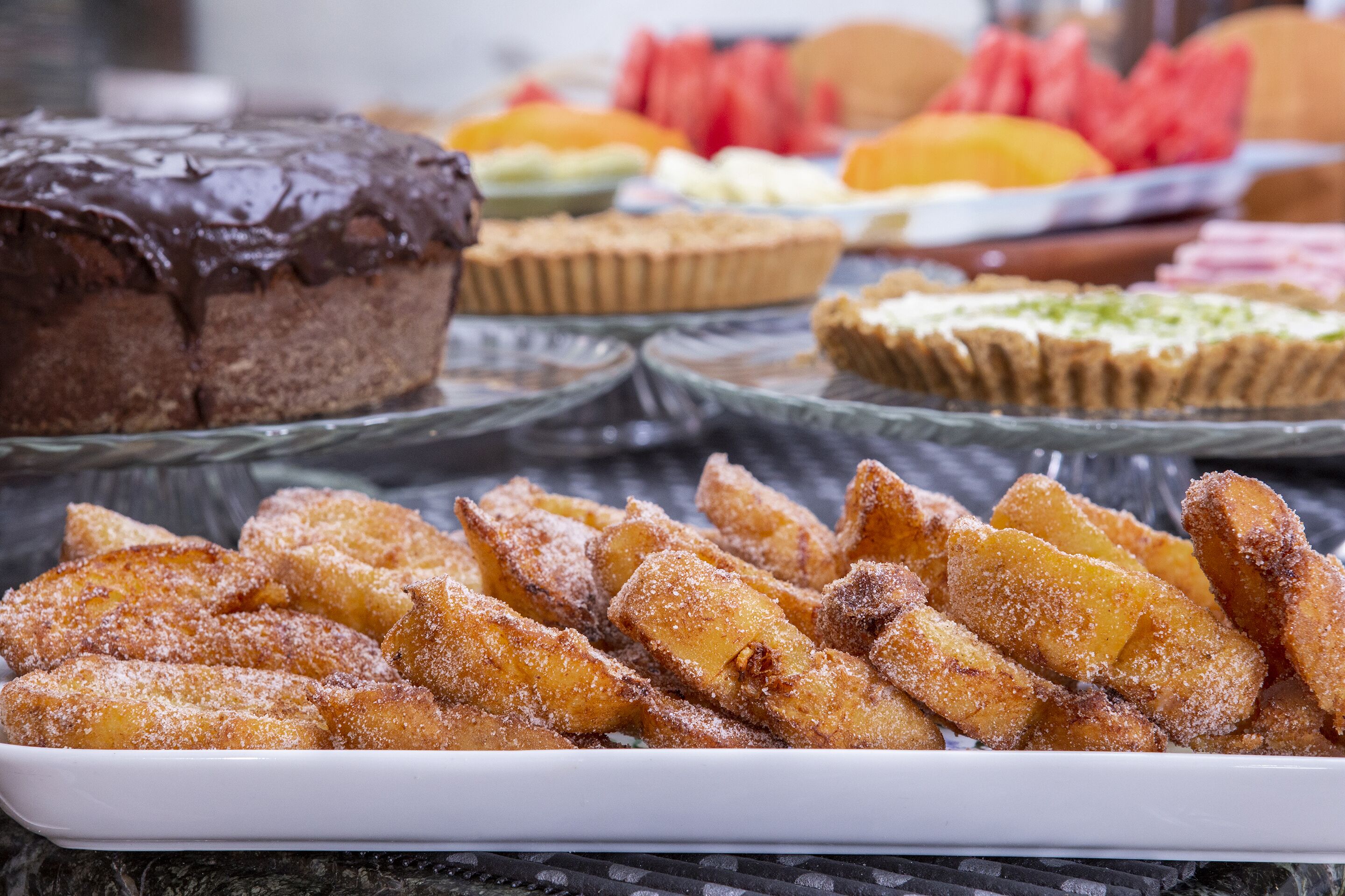 A variety of desserts on a buffet table, including a chocolate cake, fruit tarts, and sugar-dusted pastries.