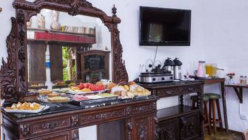 Disposição de buffet com diversas opções de comida, um espelho grande, uma televisão e uma máquina de café.