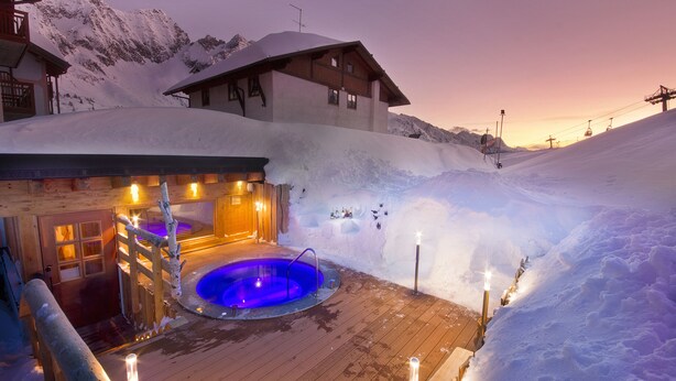 A wooden spa area with a hot tub surrounded by snow, a wooden deck, and a mountain backdrop. - Hotel La Torretta (Vermiglio)