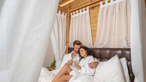 A couple in a cozy, wooden room with a canopy bed, white bedding, and a small table with a vase. - Hotel La Torretta (Vermiglio)