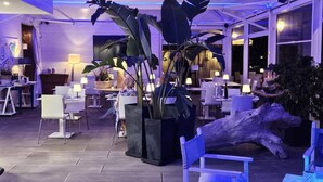 Un restaurante con mesas dentro, plantas grandes en macetas y un centro de mesa de madera.