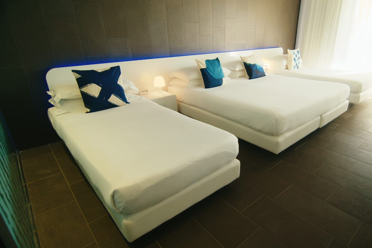 Une chambre d’hôtel avec deux lits, une tête de lit dotée d’un éclairage bleu et une vue sur l’extérieur par une fenêtre.