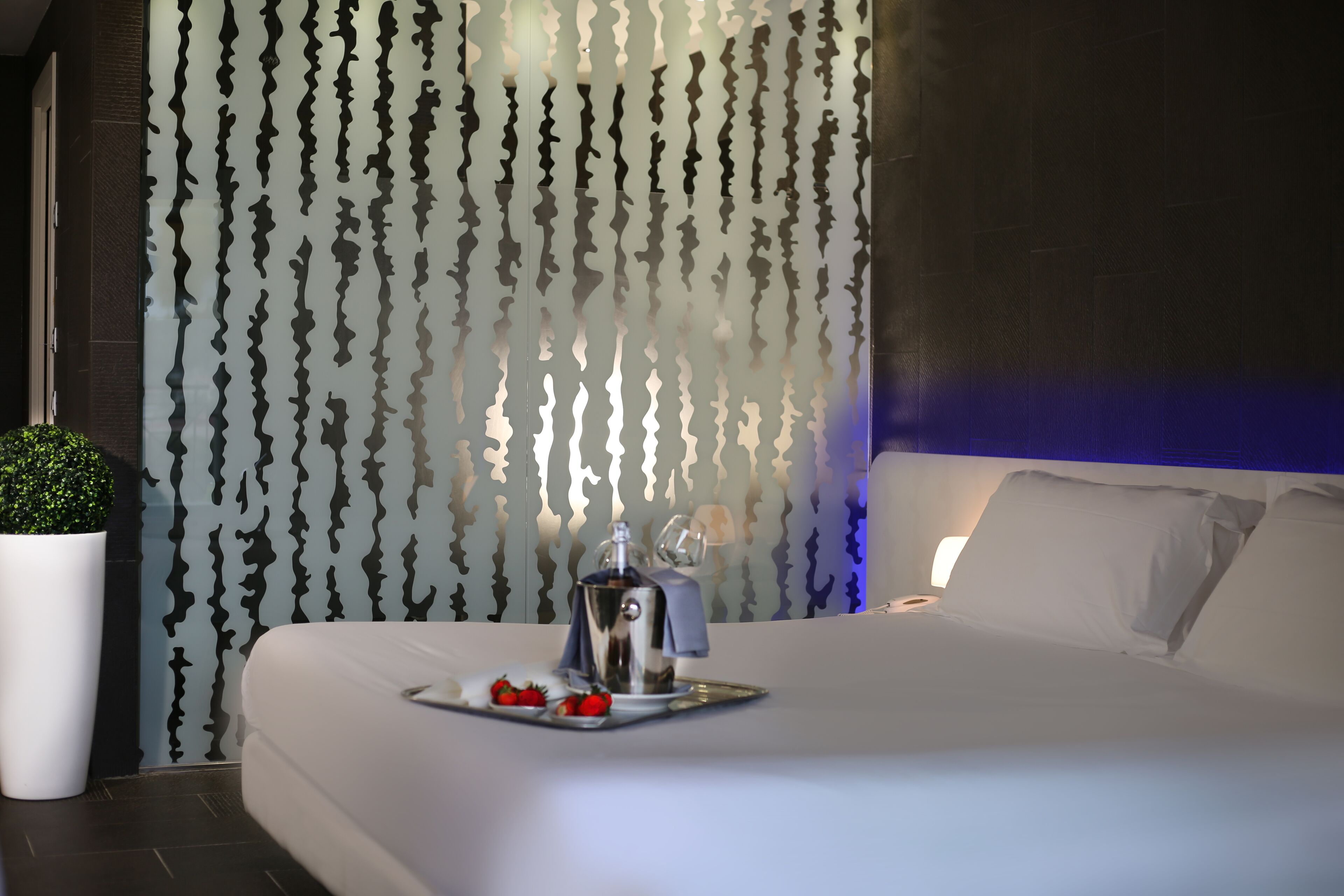 Una habitación de hotel moderna con una cama grande, una mesita de noche con cafetera y una bandeja con fresas.