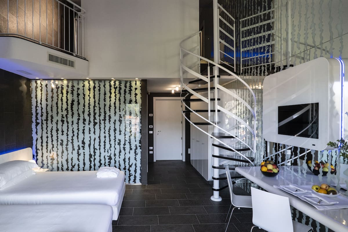 Une chambre d’hôtel moderne équipée d’un lit, d’un bureau avec des fruits, d’une télévision et d’un escalier en colimaçon.
