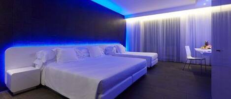 A modern hotel room with a large bed, a smaller bed, and a desk with a chair.