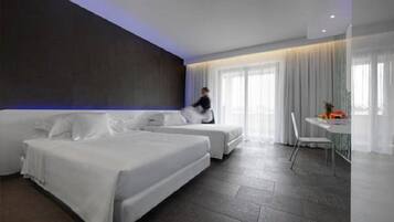 Una habitación de hotel moderna con dos camas, una zona de comedor y un ventanal con cortinas.