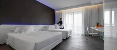 A modern hotel room with two beds, a dining area, and a large window with curtains.