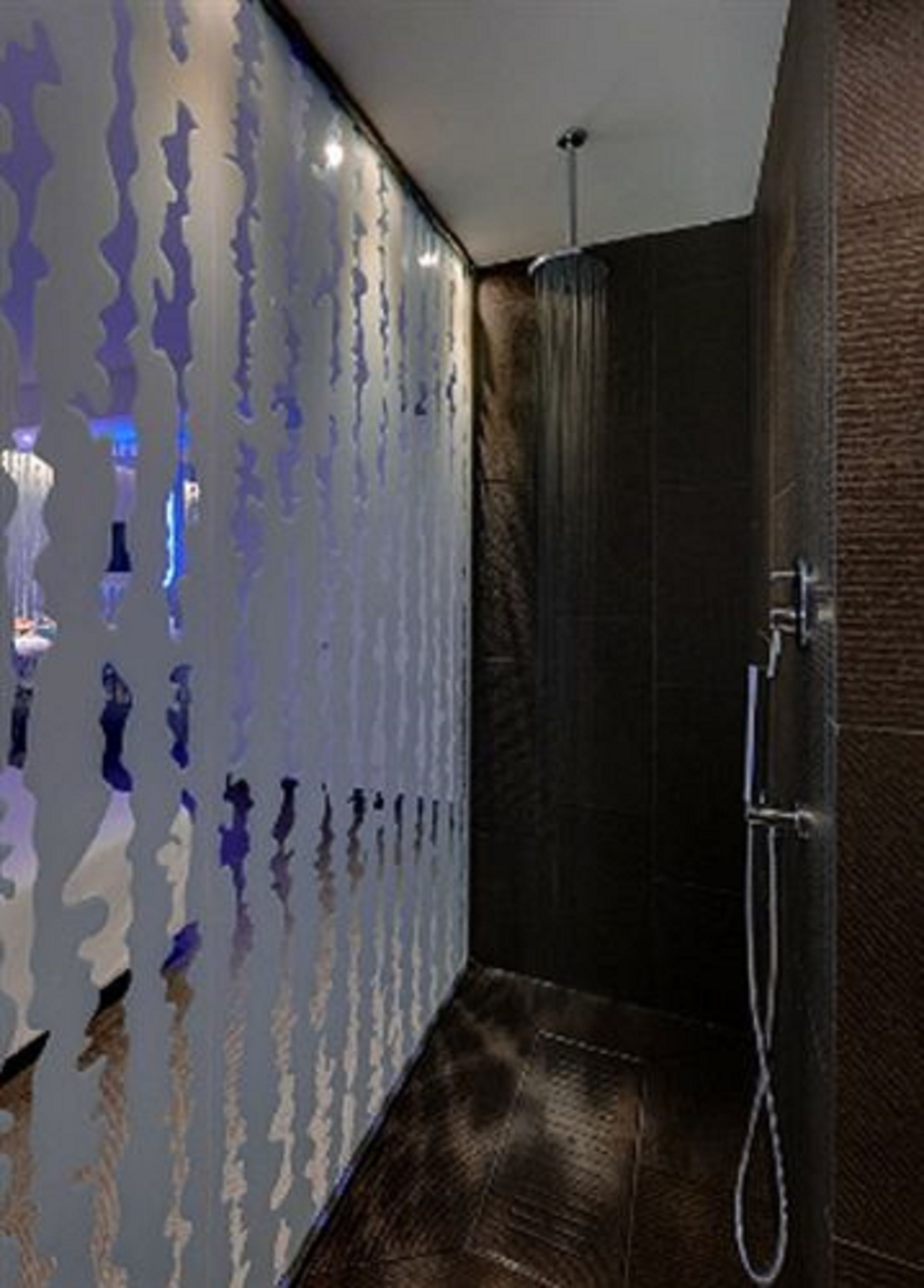 Een moderne badkamer met een douche, donkere betegelde wanden en een decoratieve muur met golvende patronen.