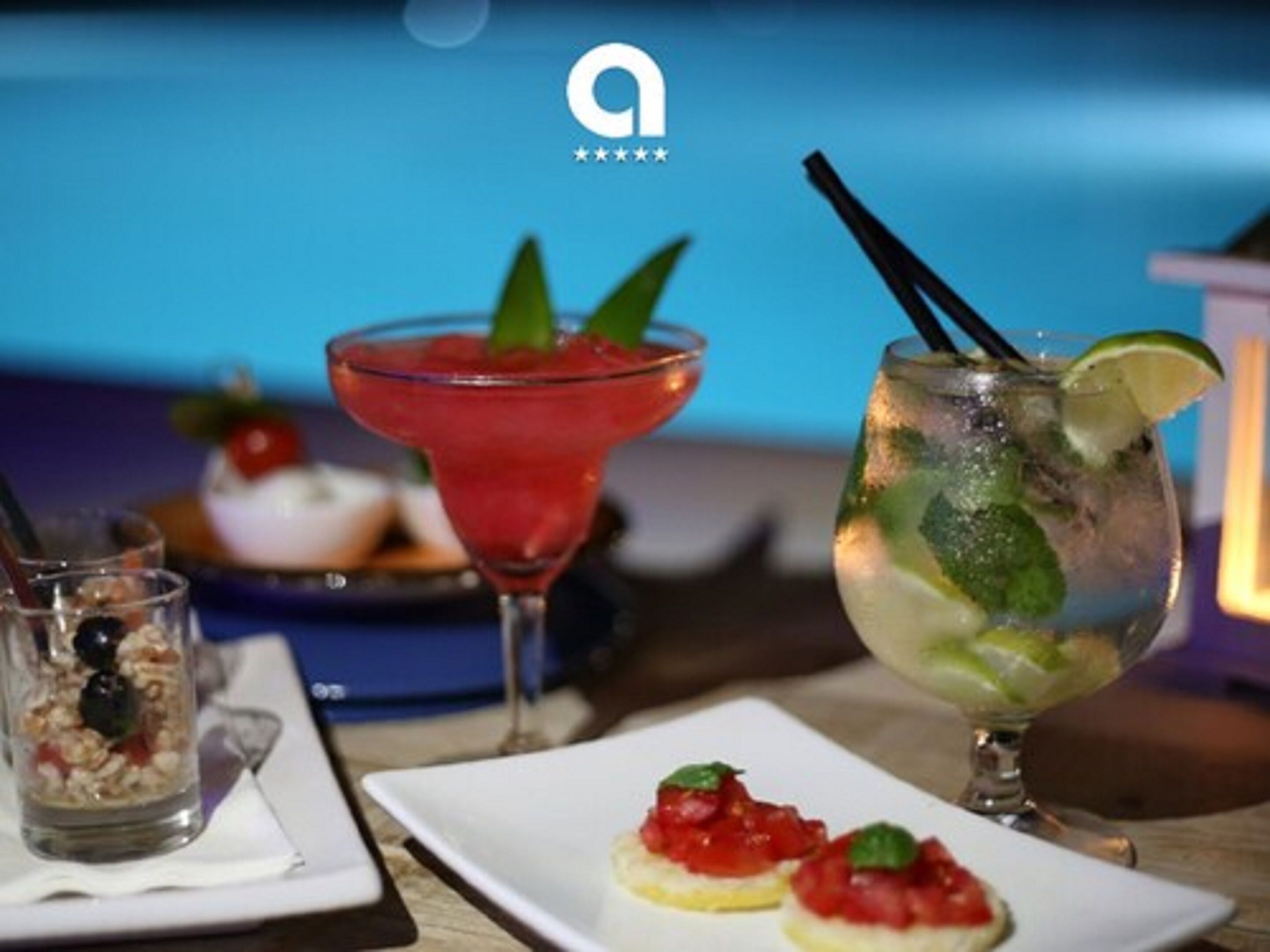 A table with a cocktail glass, a glass of iced drink with lime, and a plate with two appetizers.