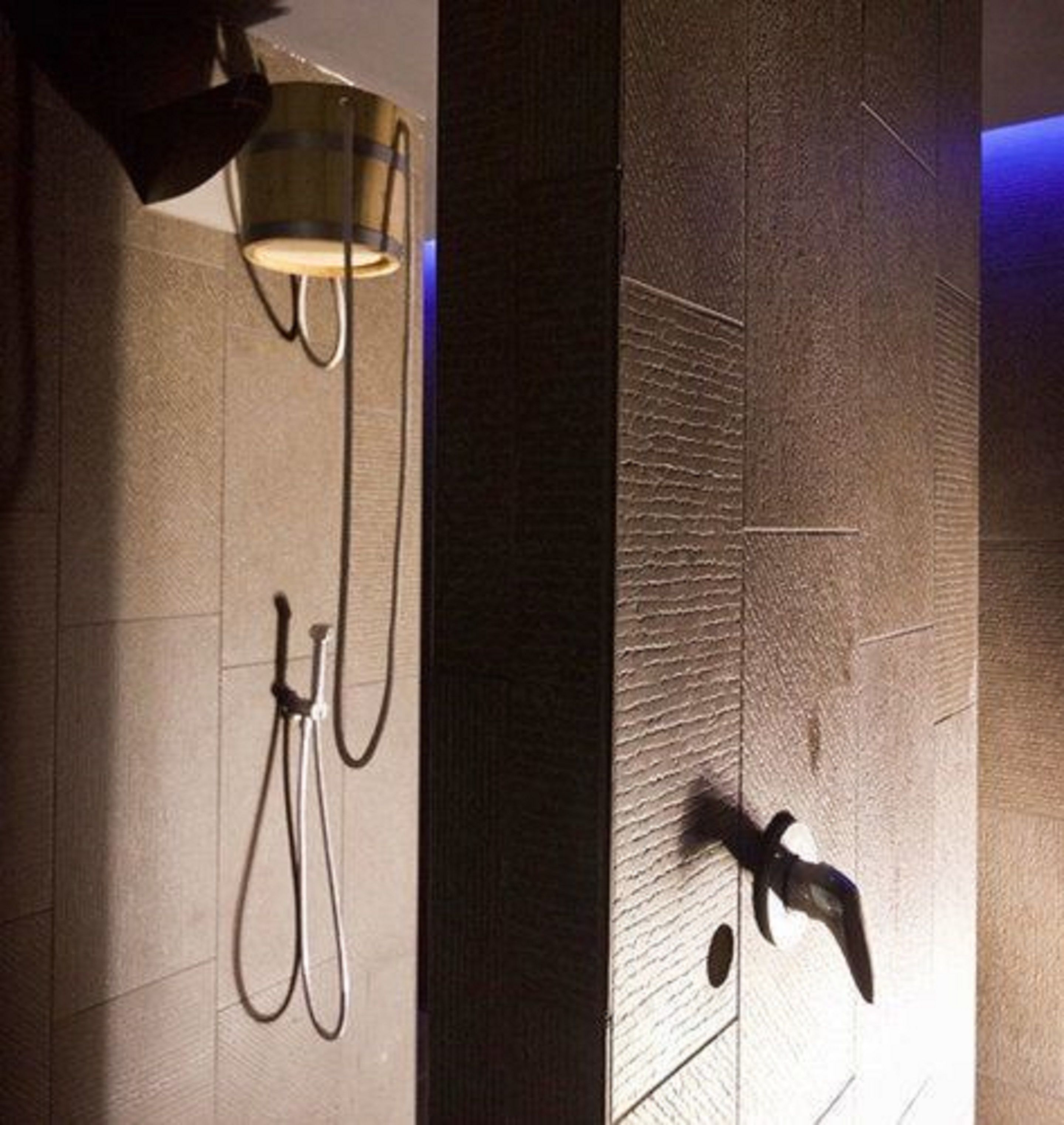 Een douchegedeelte met een handdouche en een wandlamp.