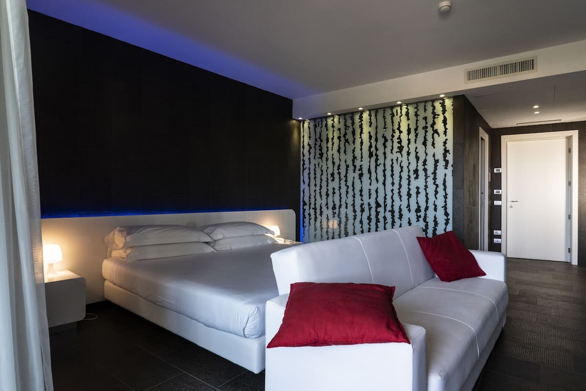 Une chambre d’hôtel moderne avec un grand lit, un canapé blanc et un mur orné de motifs.