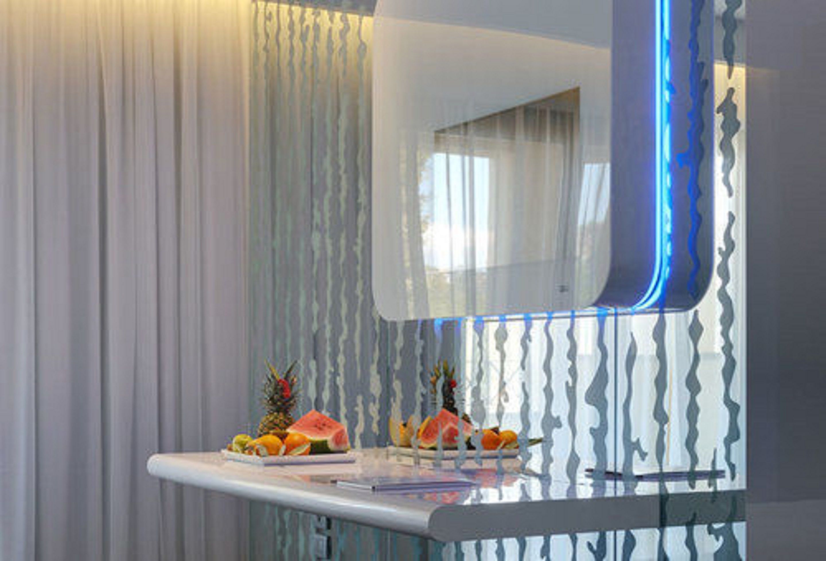 A modern room with a glass partition, a white table with fruits, and a blue light strip.