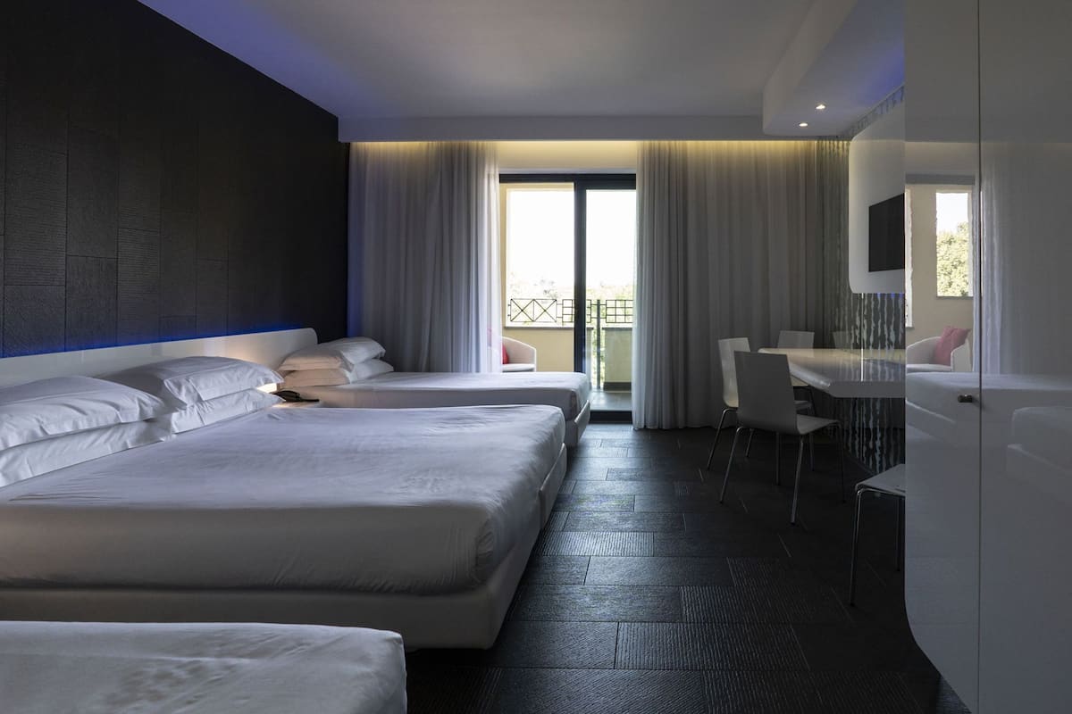 Une chambre d’hôtel avec deux lits, un bureau, une chaise, un balcon avec vue et un grand miroir.