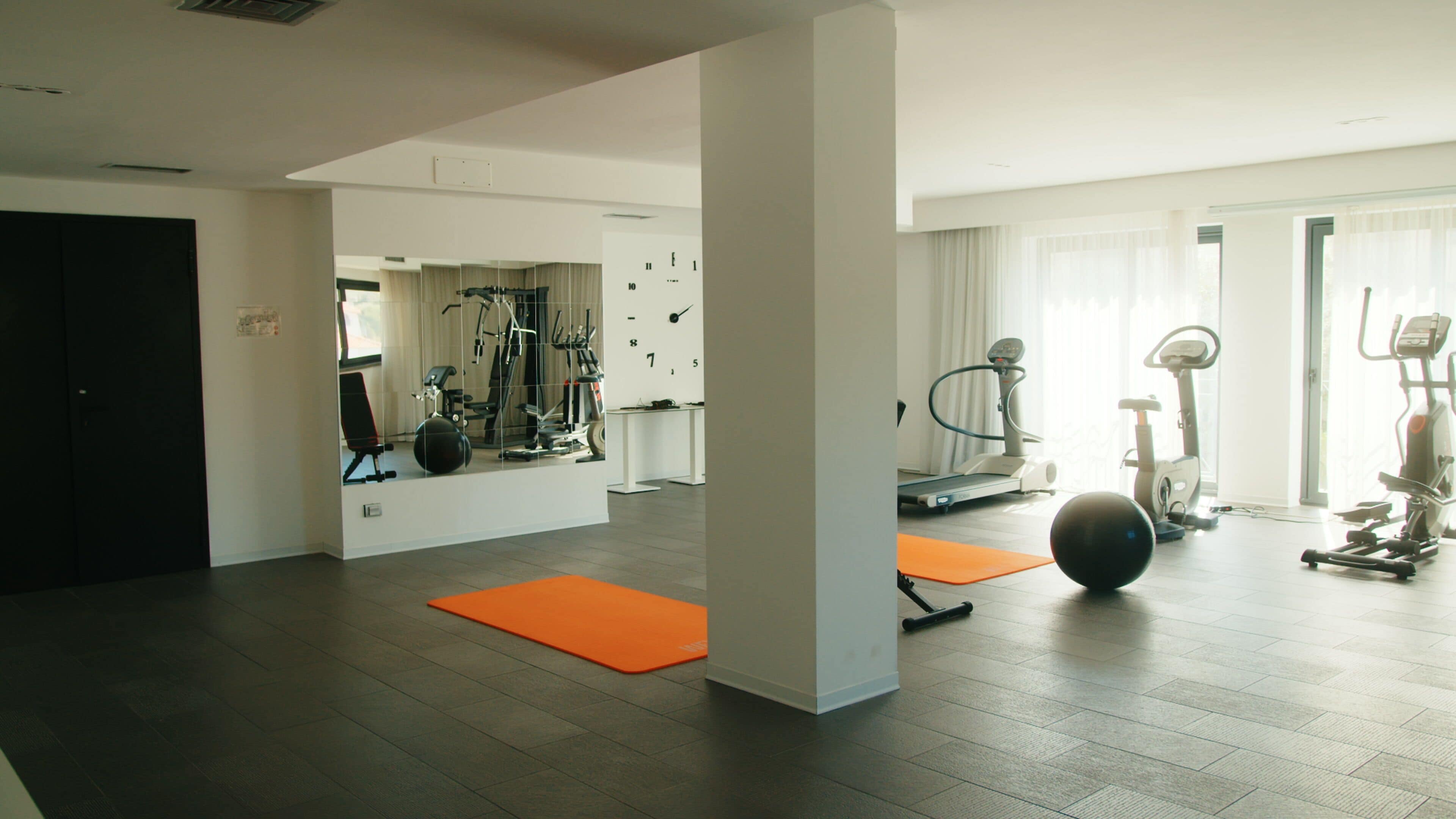 A gym with exercise equipment, a mirror, and orange mats.