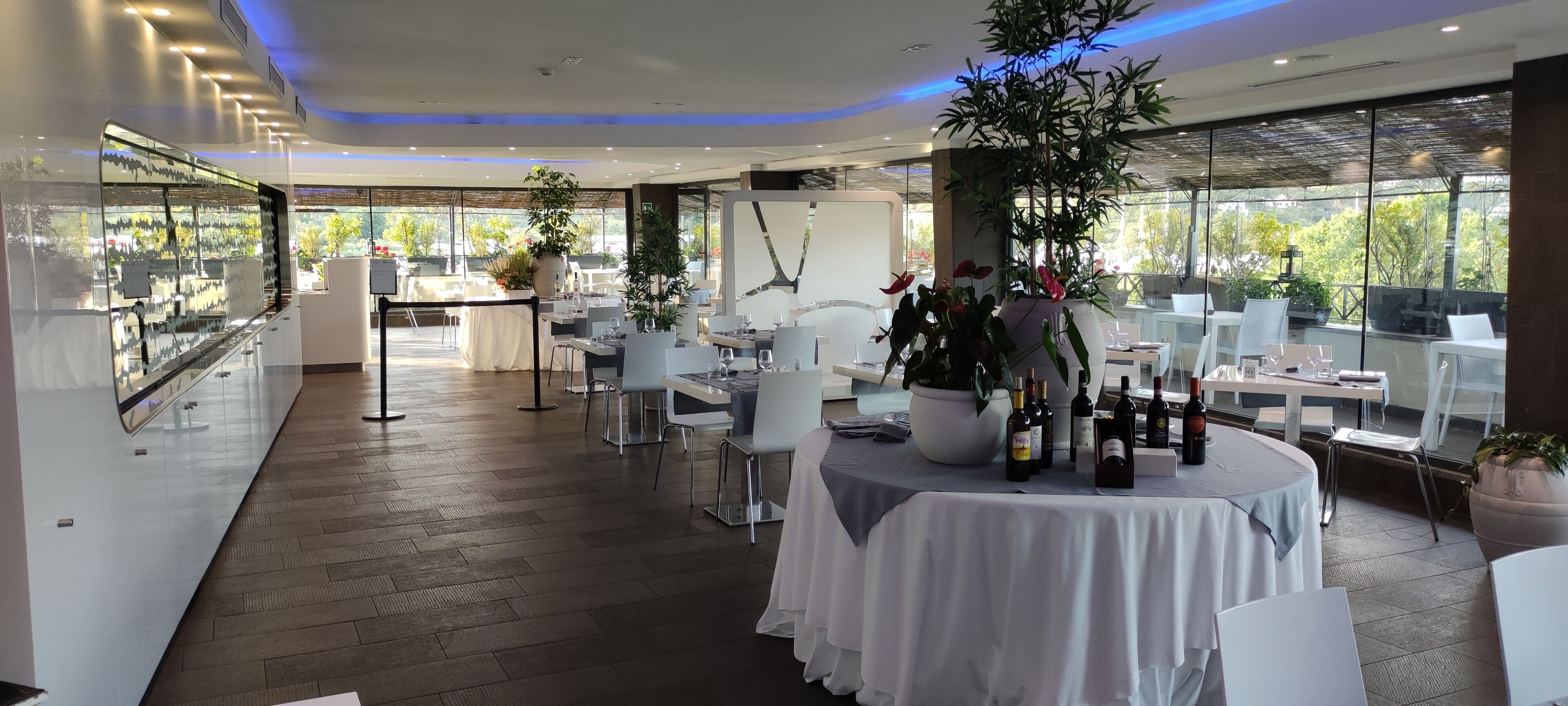 Un restaurante moderno con mesas redondas, sillas blancas y plantas en macetas.
