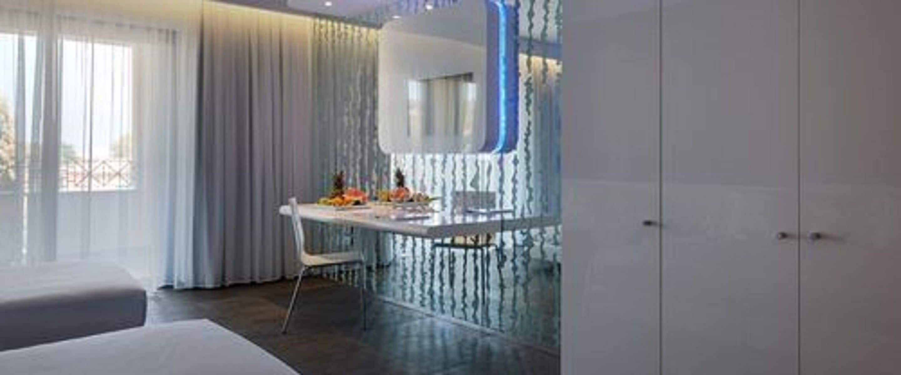 A modern bedroom with a large window, a bedside table with a lamp, and a wardrobe.