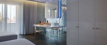 A modern bedroom with a large window, a bedside table with a lamp, and a wardrobe.
