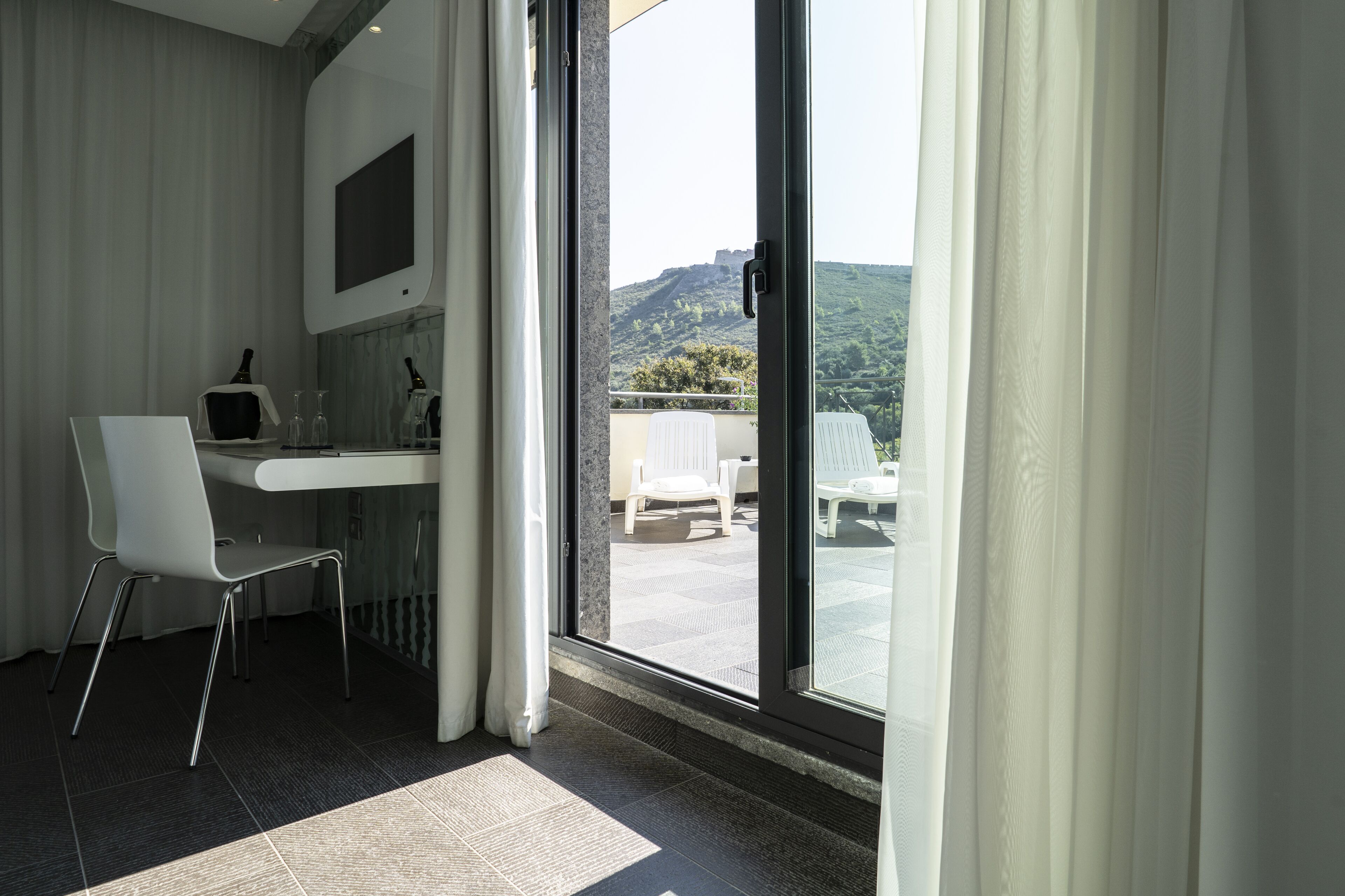 A modern room with a desk, chair, and a large sliding glass door leading to an outdoor area with chairs and a pool.