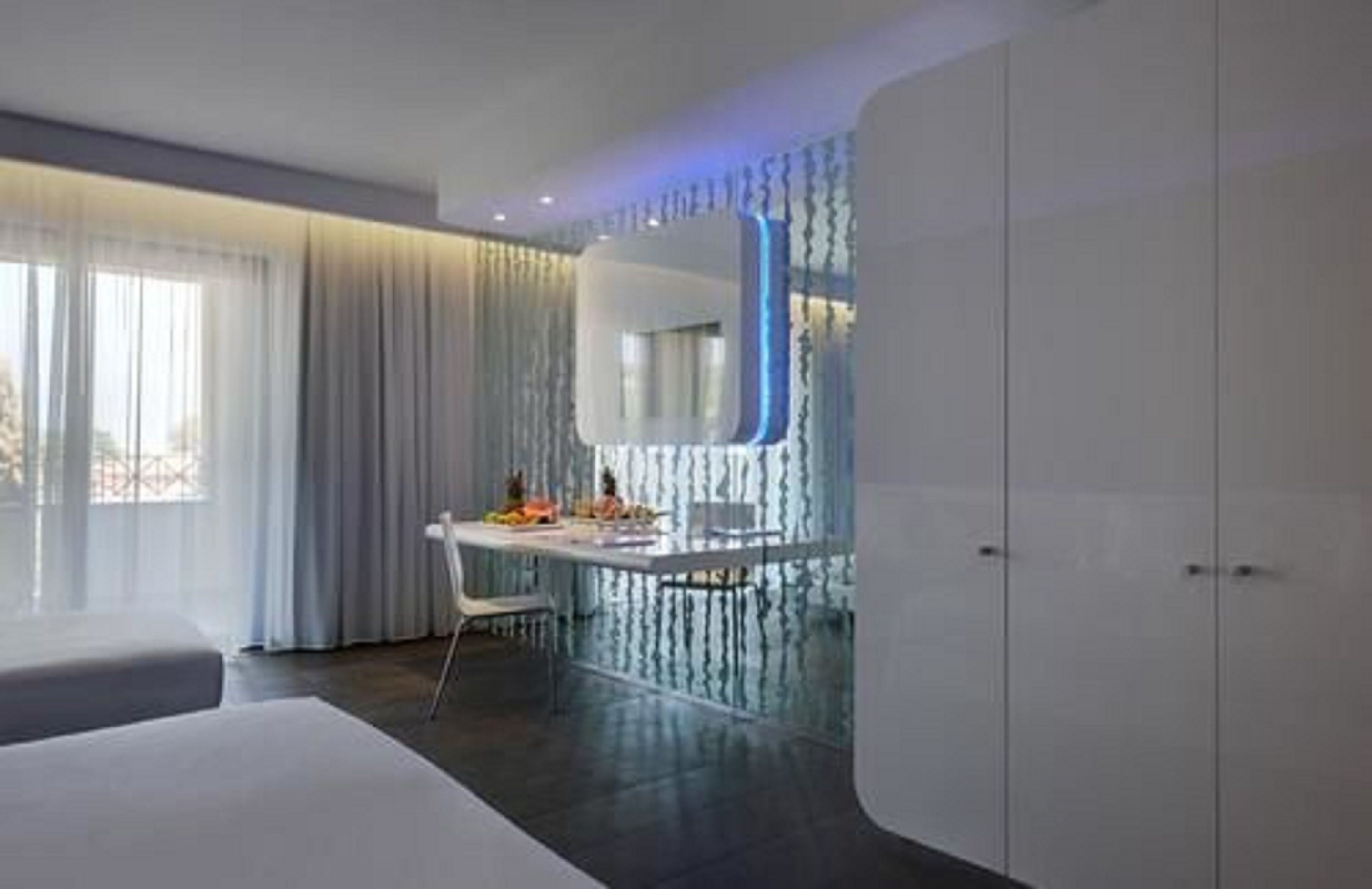 Ein modernes Hotelzimmer mit einem großen Bett, einem Schreibtisch mit Stuhl, einem Spiegel und einem Kleiderschrank.
