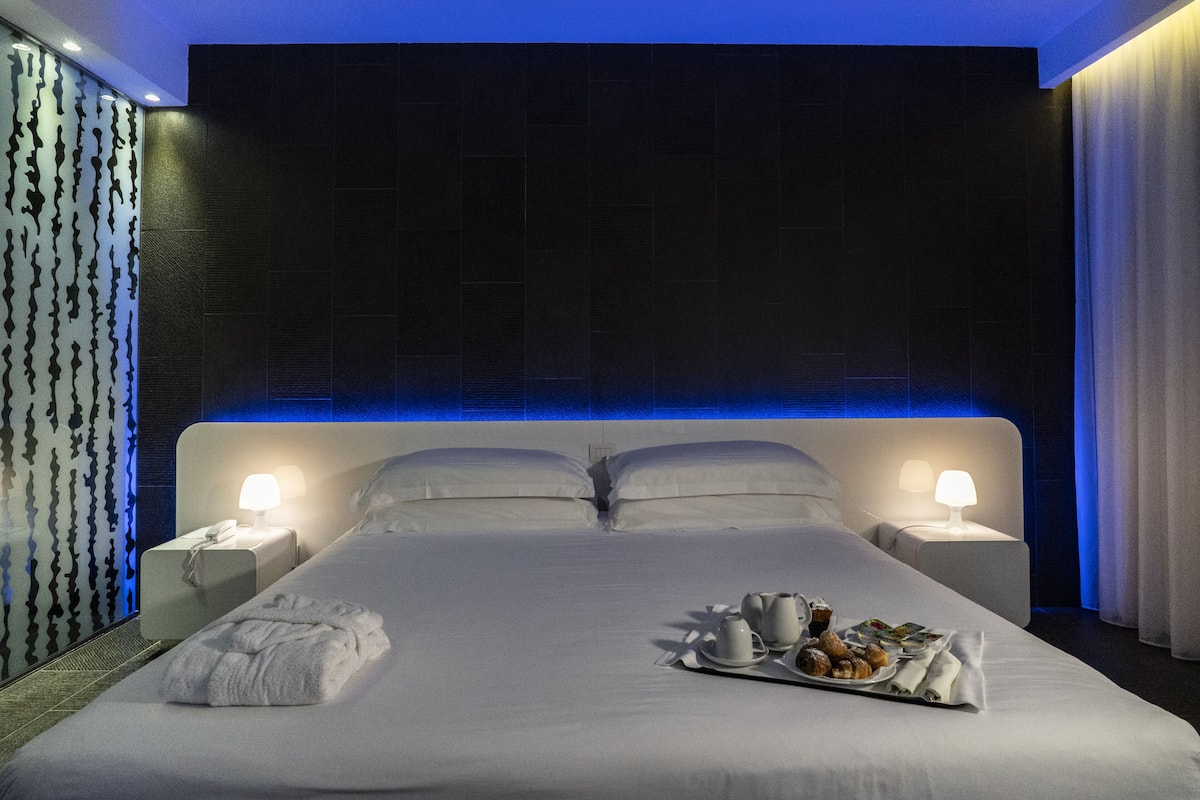 Une chambre d’hôtel avec un grand lit, deux tables de chevet et un plateau contenant des articles pour le petit-déjeuner.