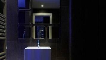 A modern bathroom with a white sink, a mirror, and a wall-mounted light fixture.