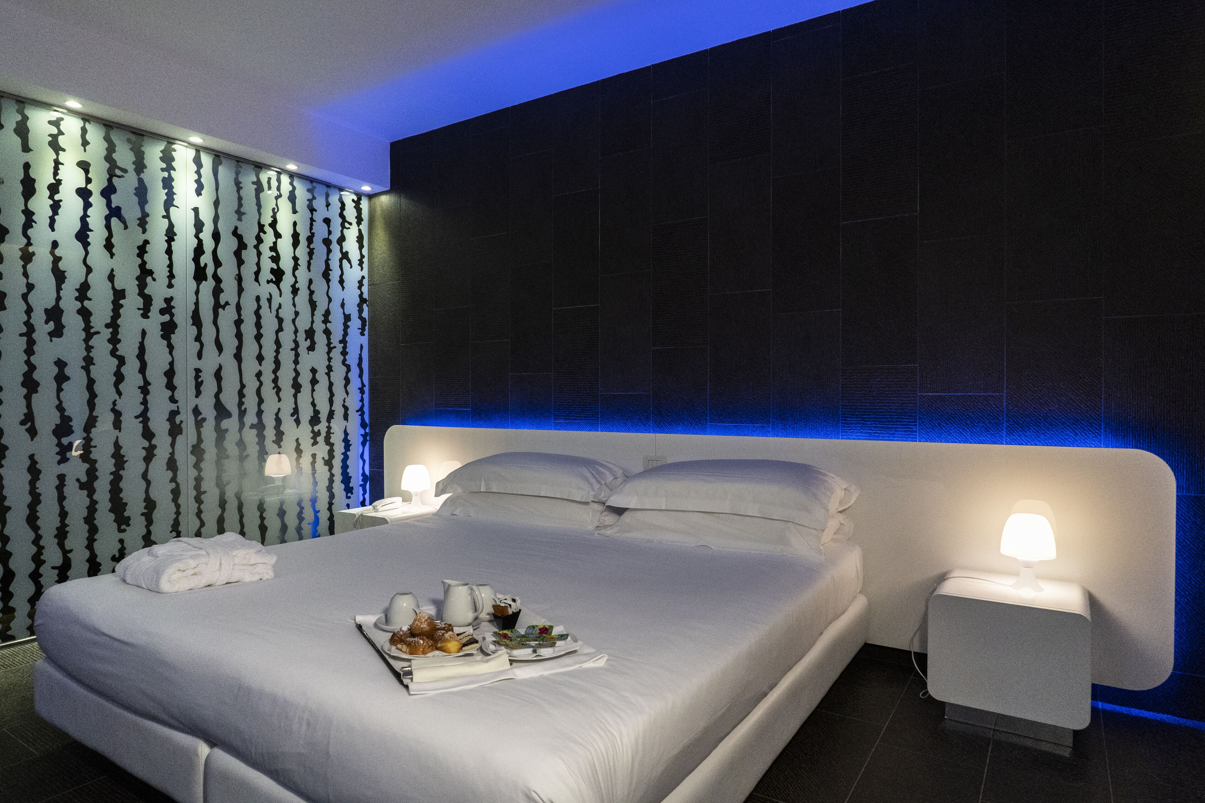 Una habitación de hotel moderna con una cama grande, mesitas de noche y un panel decorativo en la pared.