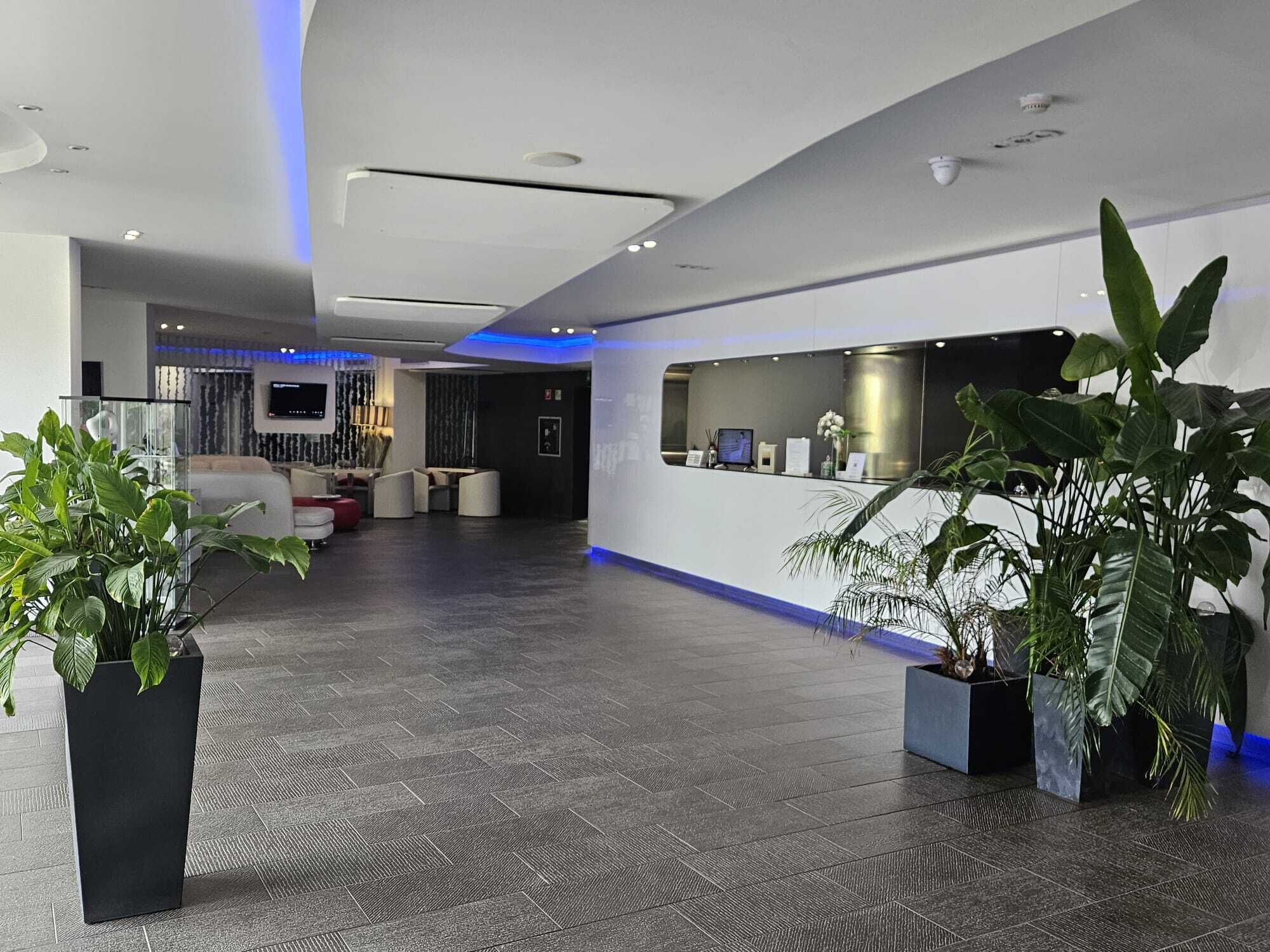 A modern hotel lobby with a reception desk, seating area, and potted plants.