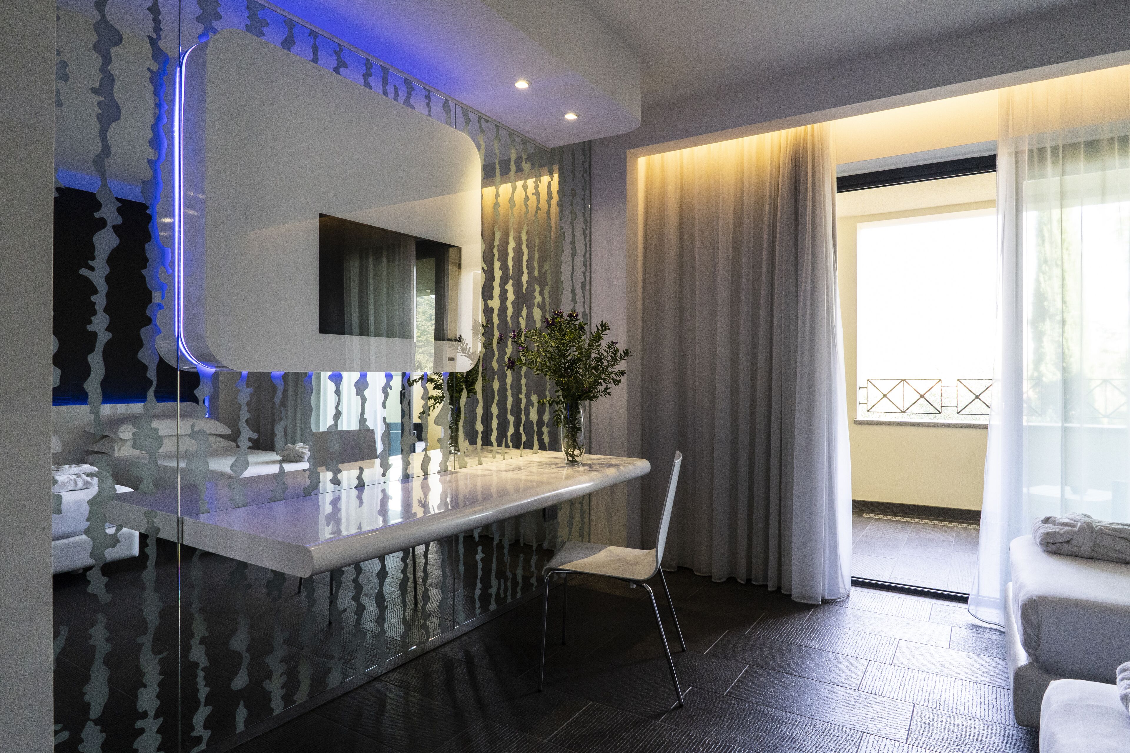 A modern bathroom with a large mirror, a vanity, a chair, and a view of the balcony.