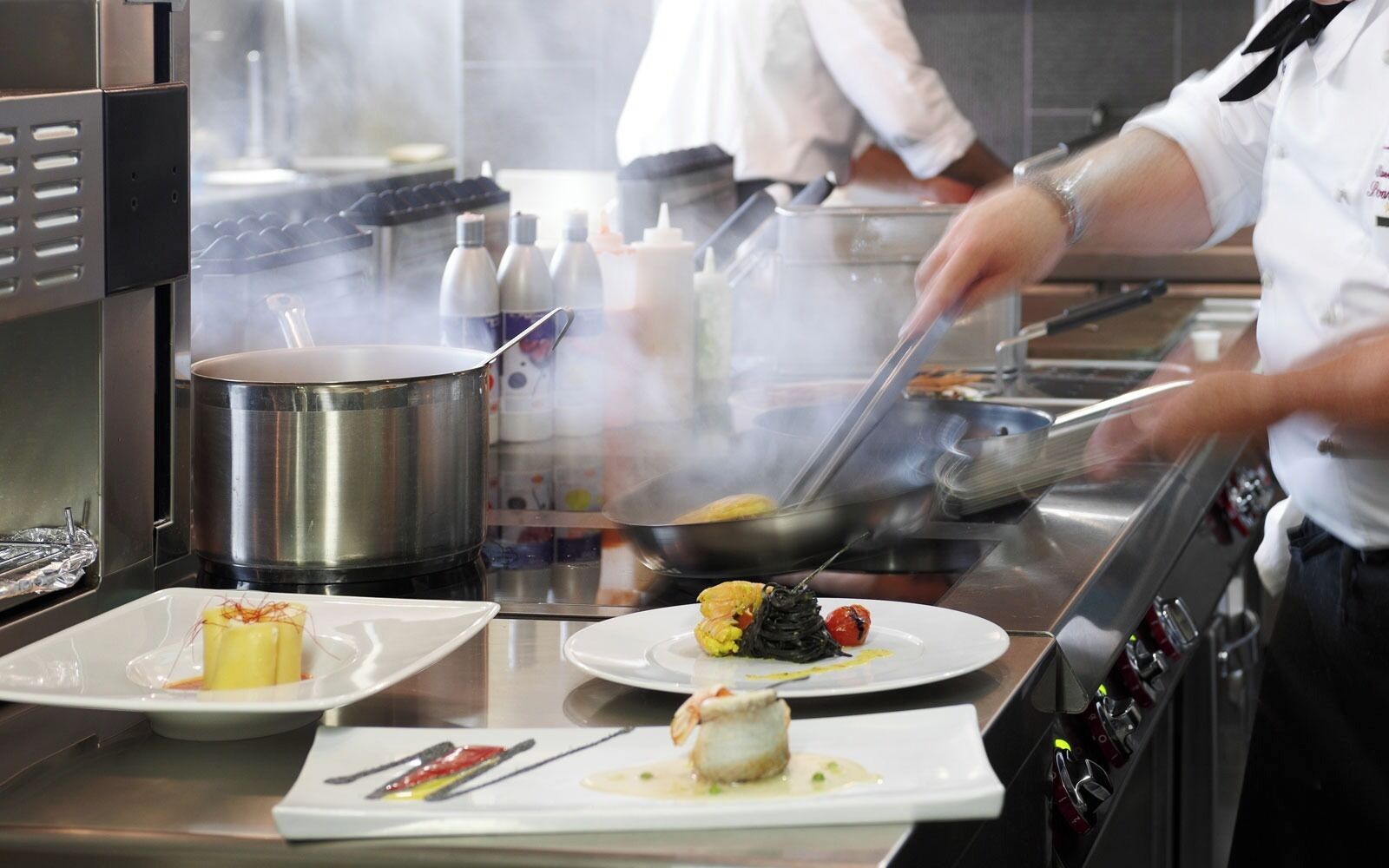 A kitchen with stainless steel appliances, a chef preparing food, and dishes on plates.
