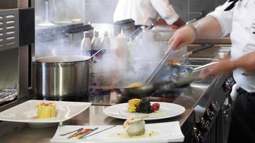 Una cocina con electrodomésticos de acero inoxidable, un chef preparando comida y platos con guarniciones.