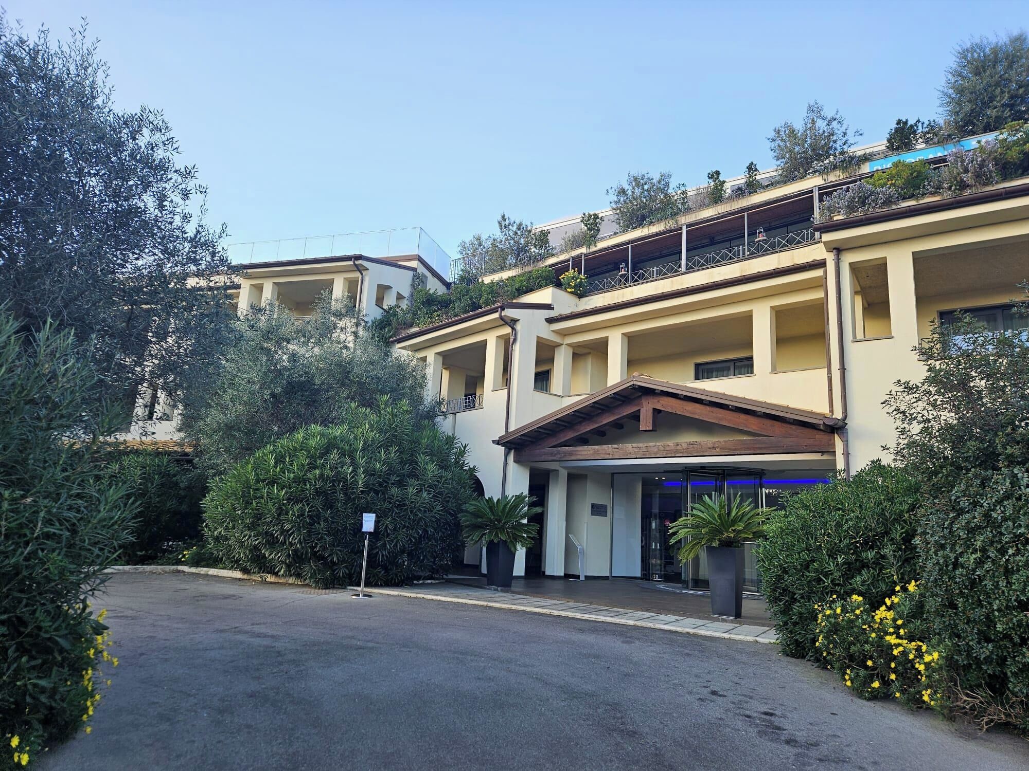 A multi-story building with a central entrance, balconies, and surrounding greenery.