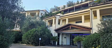 A multi-story building with a central entrance, balconies, and surrounding greenery.