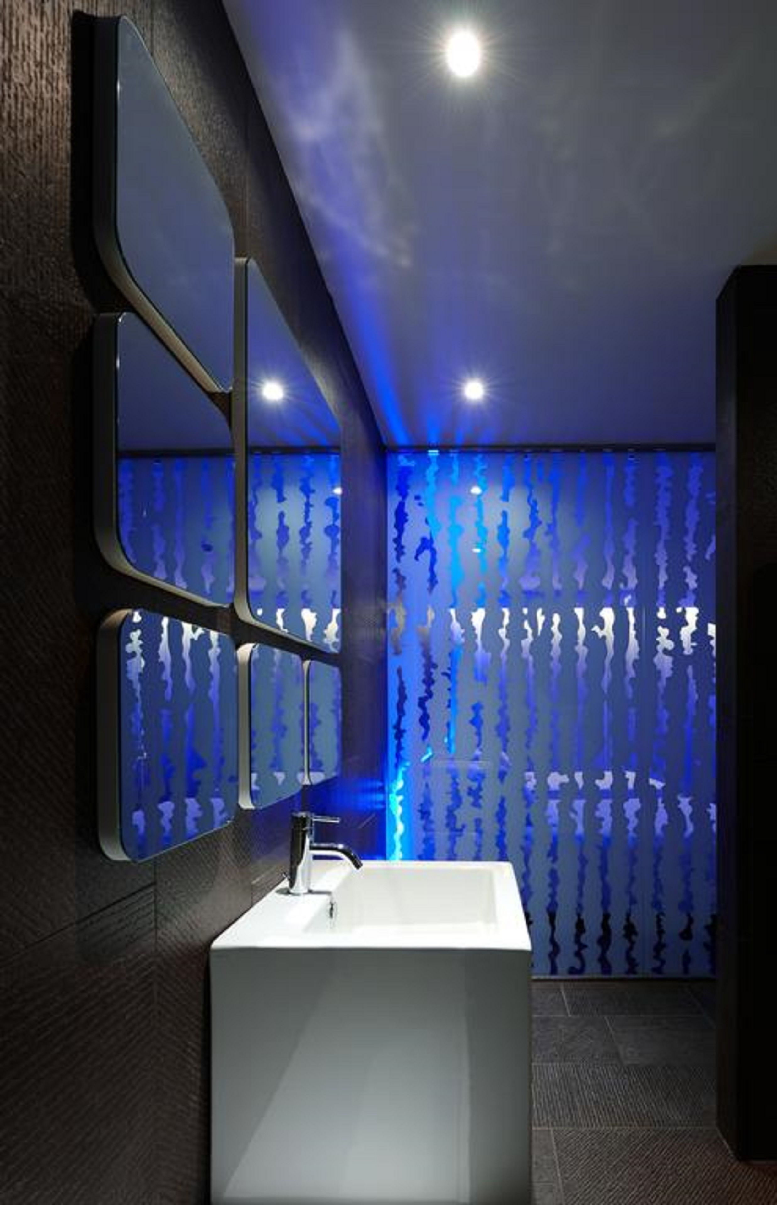A modern bathroom with a white sink, a mirror, and a wall with a blue light pattern.