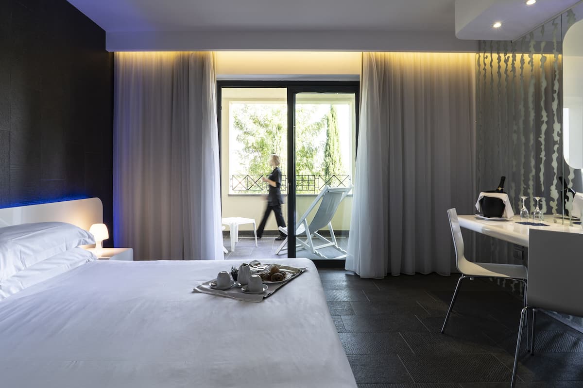Une chambre d’hôtel avec un lit, un bureau, une chaise et un balcon donnant sur la verdure.
